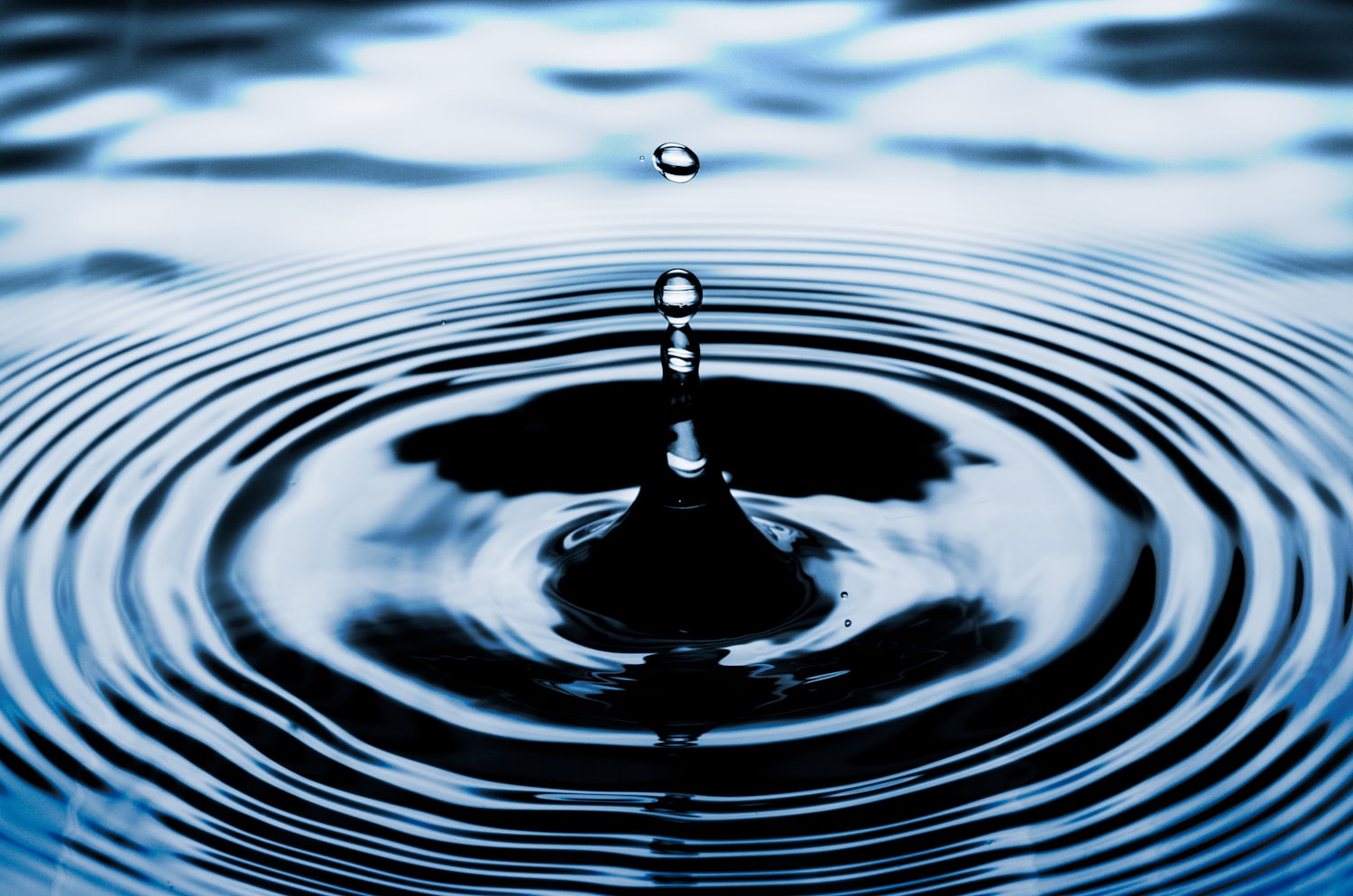 A water droplet meeting a still water surface — microbiological safety of drinking water is achieved by disinfection rather than chemical filtration.