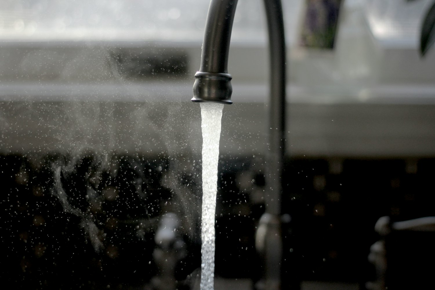 Water flowing from a kitchen faucet — flow rate, measured in gallons per minute, determines how a whole-house filter is sized to a home's demand.